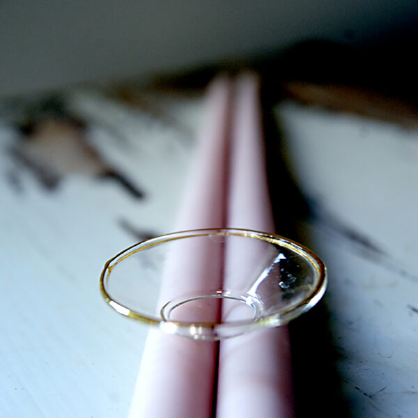 Ljusmanschett i glas med dekorativ guldig kant upptill som ligger på två rosa handstöpta ljus.