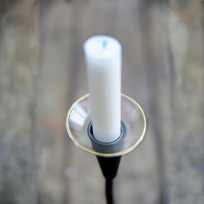 Ljusmanschett i glas med guldkant som sitter på ett vitt stearinljus i en svart smidesljusstake.