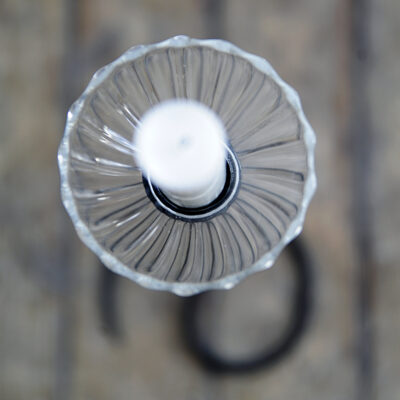 Ljusmanschett sedd uppifrån i vågigt glas på ett vitt ljus i en svart smidesljusstake.