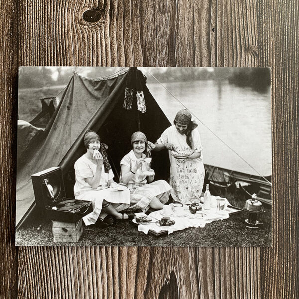 Vykort med svartvitt motiv från 1930-talet som föreställer tre vänner som har picknick utanför sitt tält.