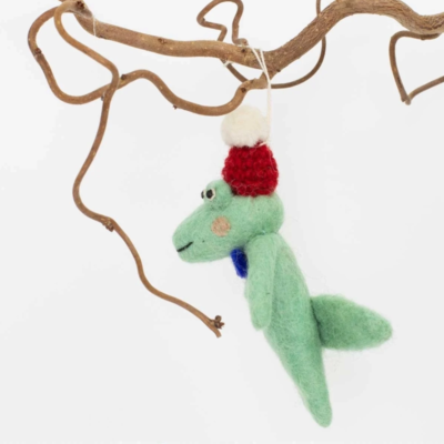 Julgranshänge i form av en tovad grön ullkrokodil med röd mössa och blå fluga som hänger på en gren i profilbild.