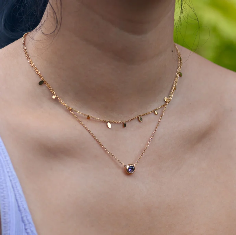 Närbild på halsband på en kvinna som visar två guldhalsband med berlocker.