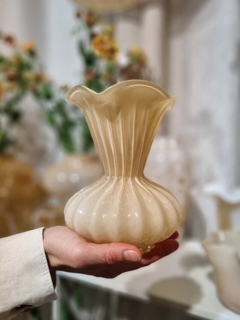 Cremefärgad romantisk glasvas som någon håller i en hand.