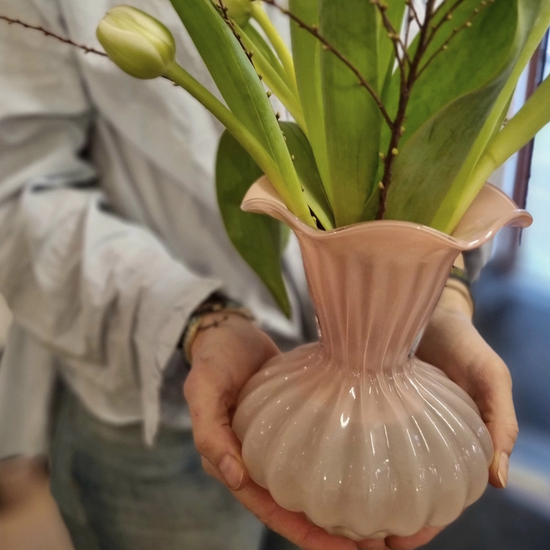 Rosa romantisk glasvas med tulpaner i som någon håller i bägge händerna.