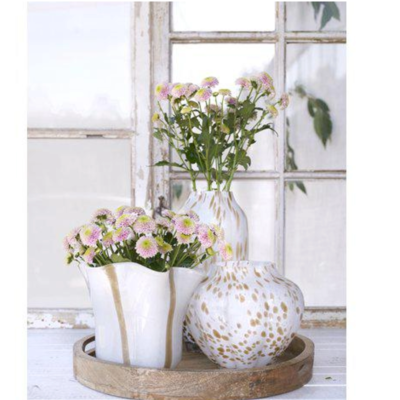 Tre vita glasvaser i olika storlekar med beige detaljer med blommor i, ståendes på en träbricka.